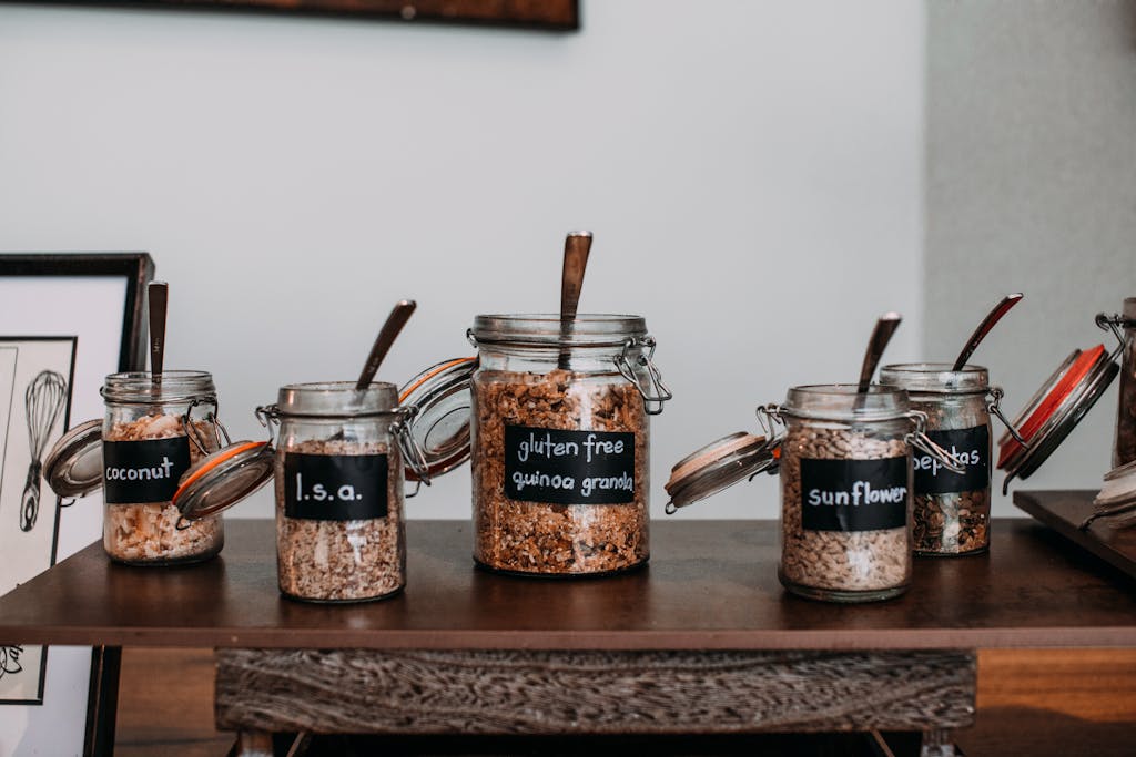 Close-up of labeled glass jars containing various grains and seeds on a wooden table.